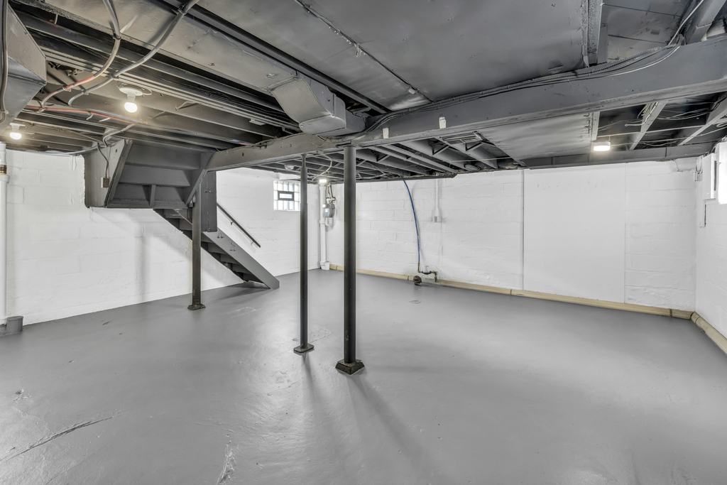 An unfinished basement with exposed joists, steel posts and stairs