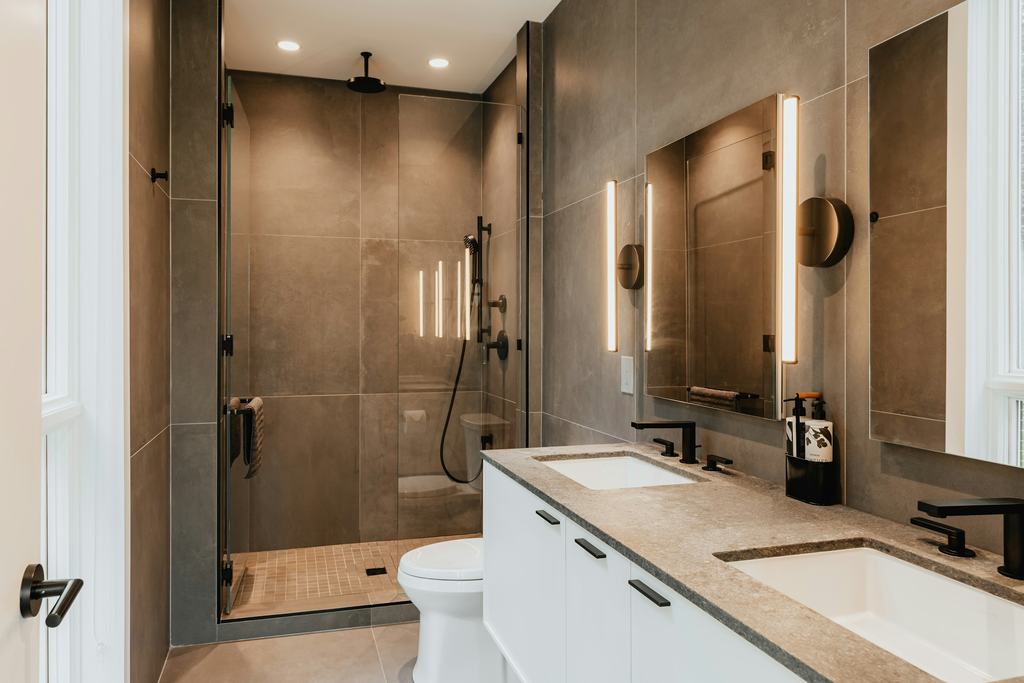 A modern bathroom with a glass shower, dark tile and a double vanity (illustrative)