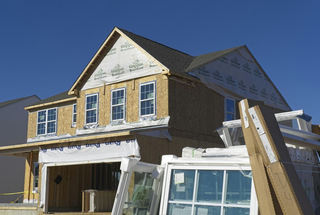 A two-storey house under construction with sheathing and stacked new windows (illustrative)